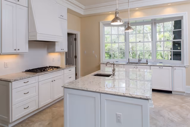Bright white kitchen with a large center island, granite countertops, gas cooktop, and a wall of windows.