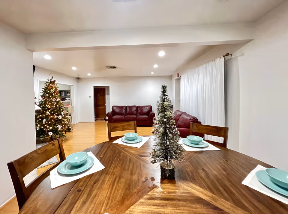 A dining table set with turquoise dishes and a small decorative Christmas tree, overlooking a living room with red sofas and a decorated Christmas tree.