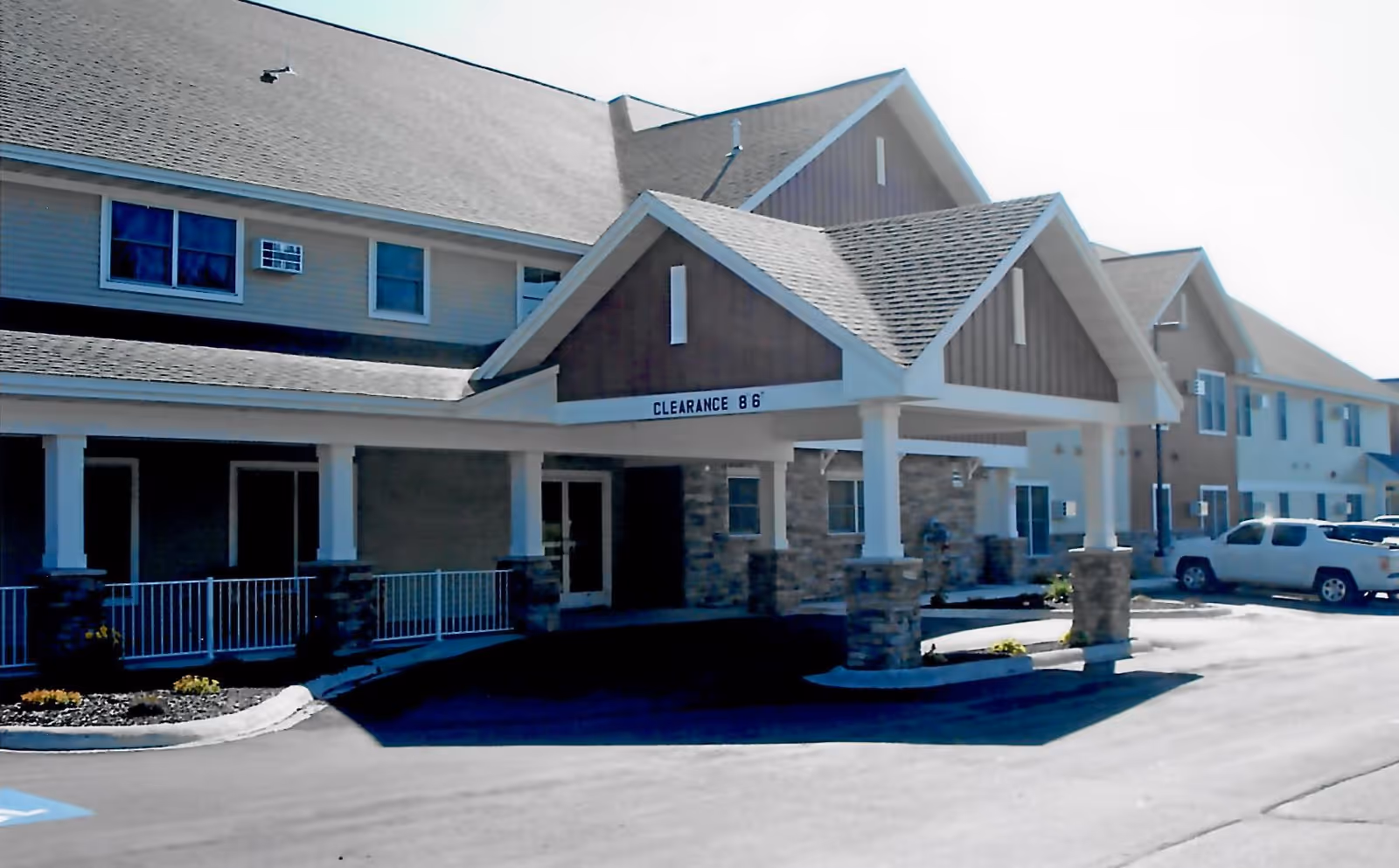 Exterior front entrance of a two-story senior living building with a covered drive-through entrance and stone columns.
