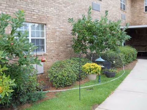 Brick exterior of a building with windows and well-kept shrubs along a walkway.