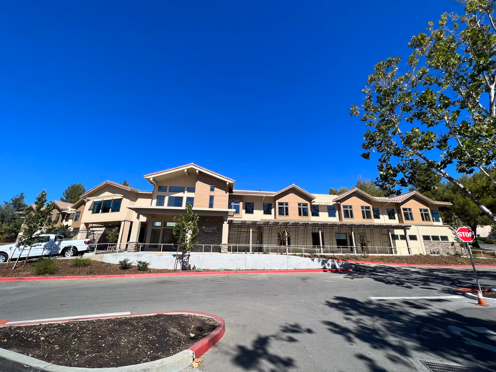 Front exterior of a tan, multi-wing senior living building against a blue sky