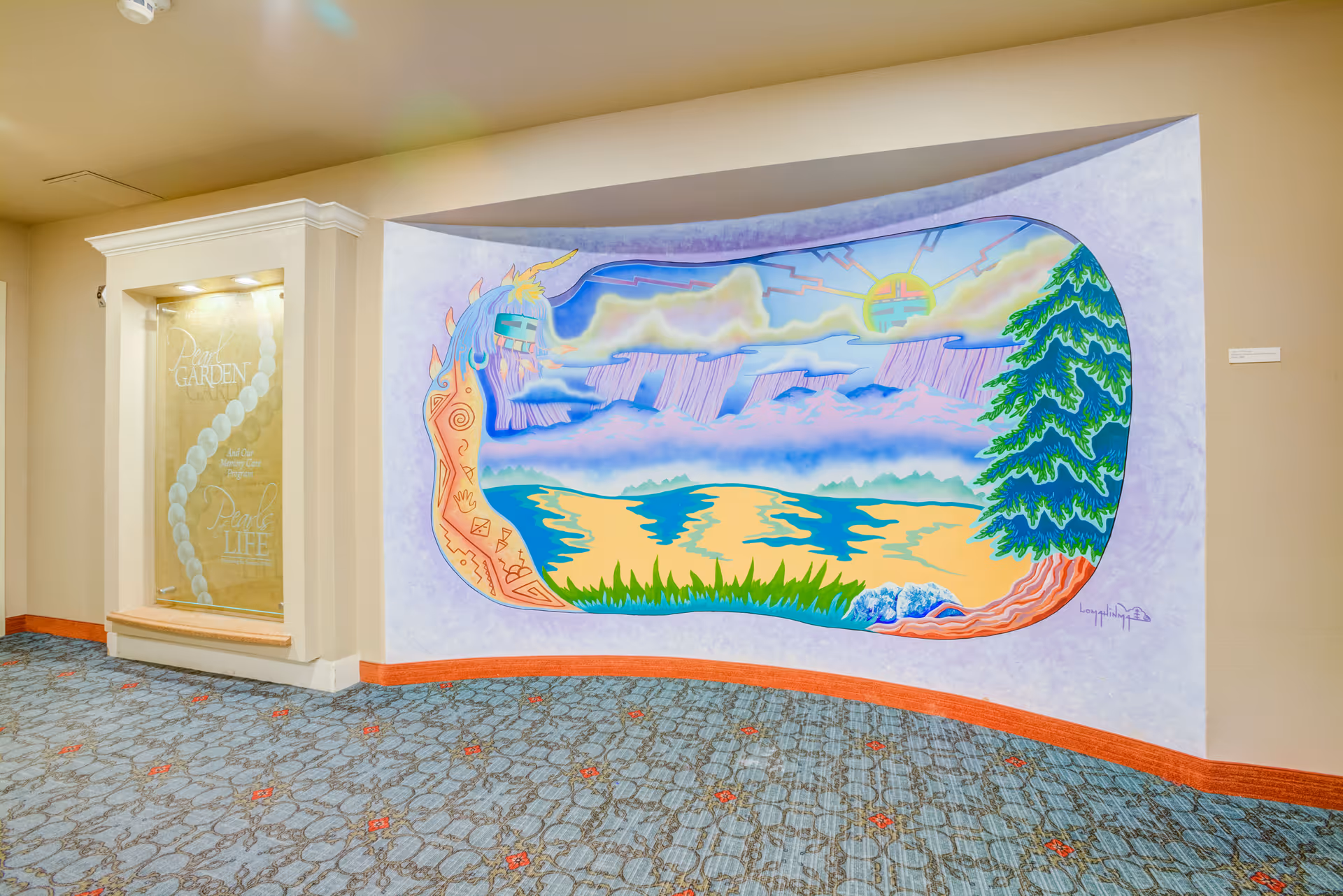 A hallway interior with a colorful mural on the wall depicting a stylized landscape with a sun, clouds, water, grass, and a tree. To the left of the mural is a display case with the words 'People GARDEN' and 'People LIFE' etched on glass. The floor is carpeted with a patterned design.