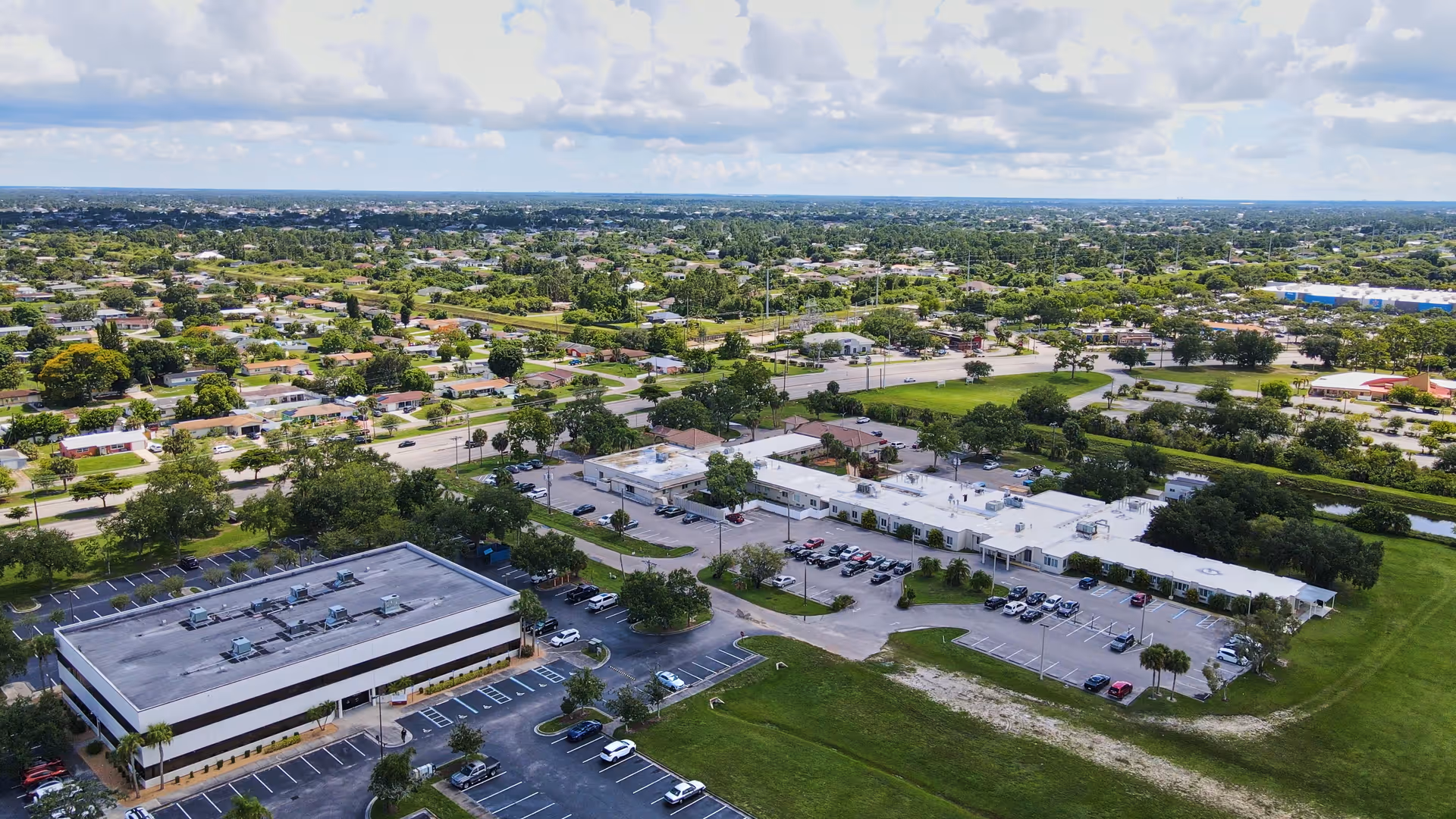 Aerial view of a senior living facility campus with multiple low-rise buildings, parking lots, and surrounding residential neighborhood.
