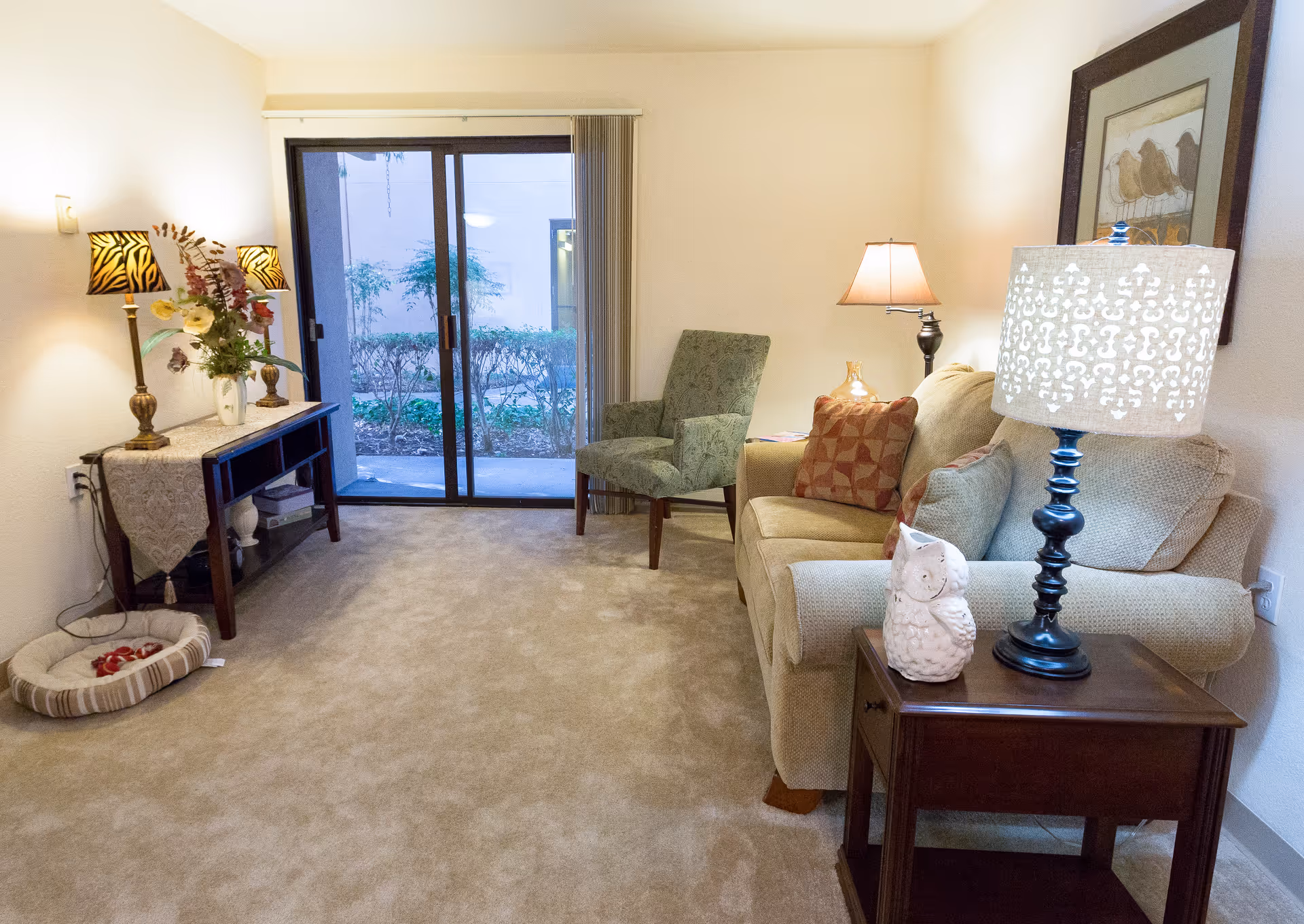 Cozy living room with a sofa, armchair, side tables and lamps, sliding glass doors to an outdoor area, and decorative accents.
