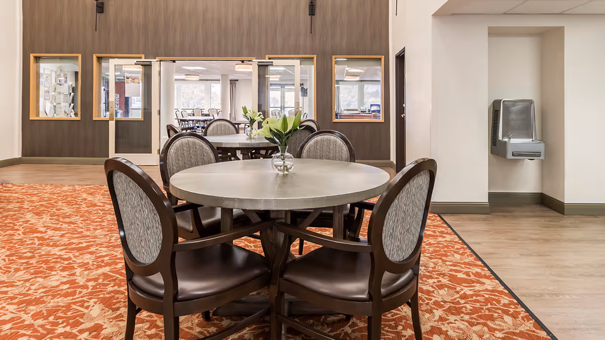 Round dining table with a small vase of flowers and chairs in a retirement community common dining area.
