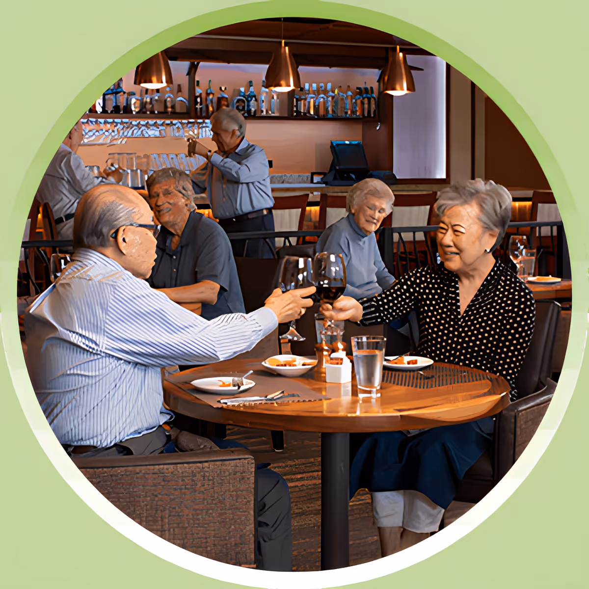 Two elderly people sitting at a round wooden table in a restaurant or dining area, clinking wine glasses and smiling. In the background, other elderly individuals are seated and a bartender is preparing drinks behind a bar with shelves of bottles and glasses.