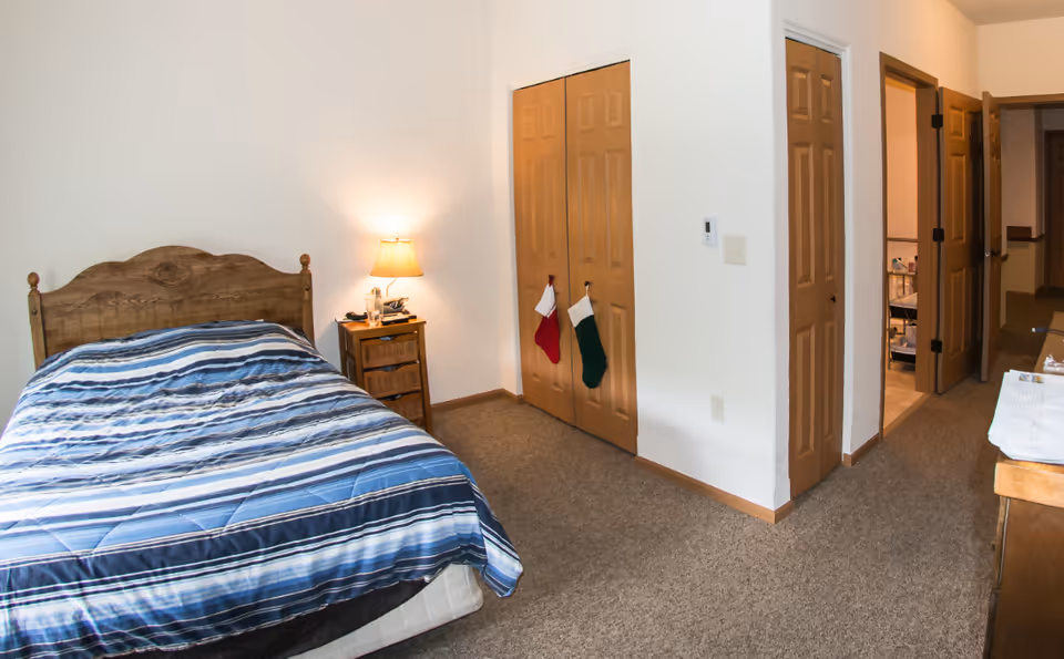 A bedroom with a blue-striped bed, nightstand, lamp, and closet doors.