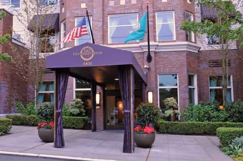 Brick senior living facility entrance with purple canopy, flags, and manicured landscaping.