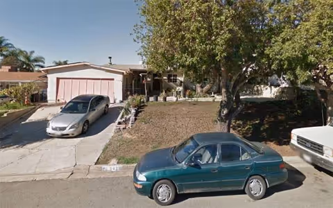 Exterior view of Casa Primavera senior living facility with parked cars and a large tree.