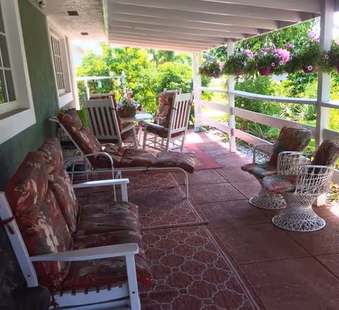 Covered outdoor porch with wicker chairs, cushioned seating, and hanging flower baskets.