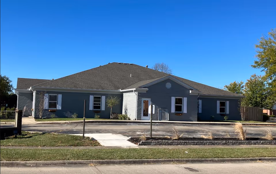 Single-story blue-gray assisted living building with front entrance and sidewalk.