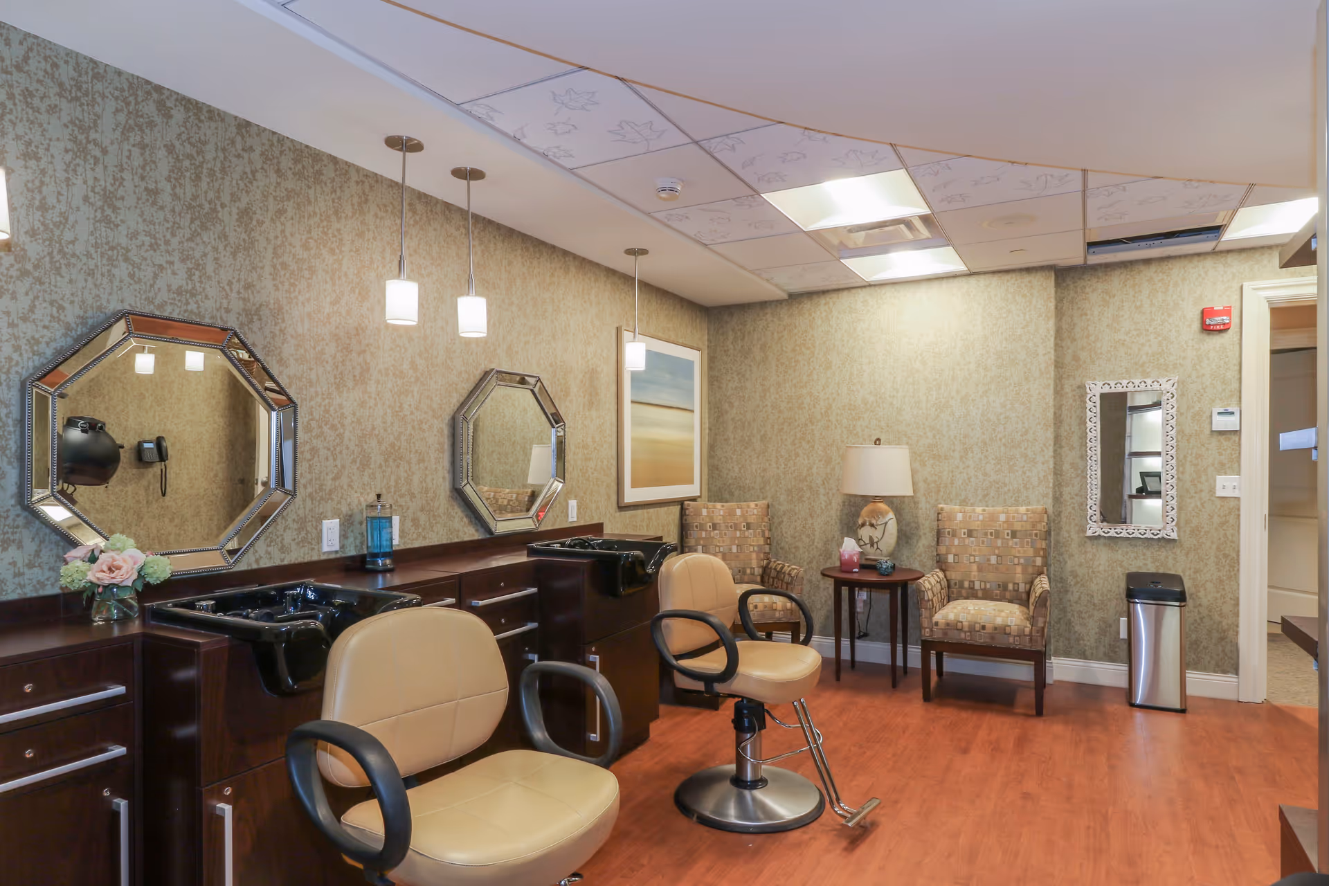 Interior salon with styling chairs, wash sinks and octagonal mirrors, plus a small seating area with armchairs and a side table.