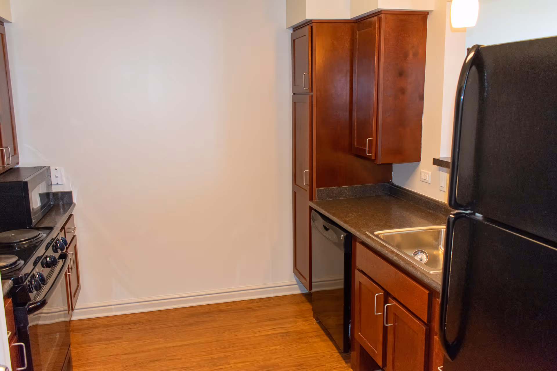 A compact kitchen featuring dark wood cabinets, black refrigerator and stove, a sink, dishwasher and laminate countertops.