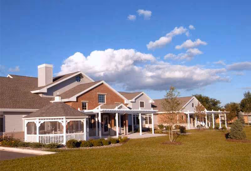 Rennes Health & Rehab Center De Pere exterior brick building with white pergolas and lawn.