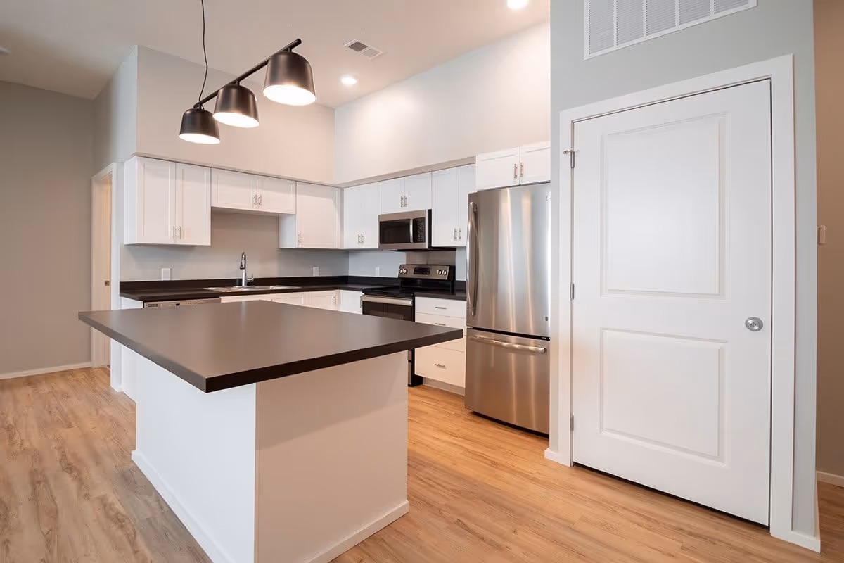 Modern kitchen with a large dark-topped island, white cabinets, stainless steel appliances, and hanging pendant lights.