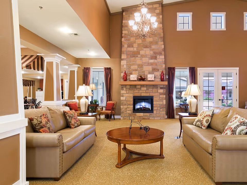 Spacious living room with two leather sofas facing a round wooden coffee table and a stone fireplace topped by a chandelier.