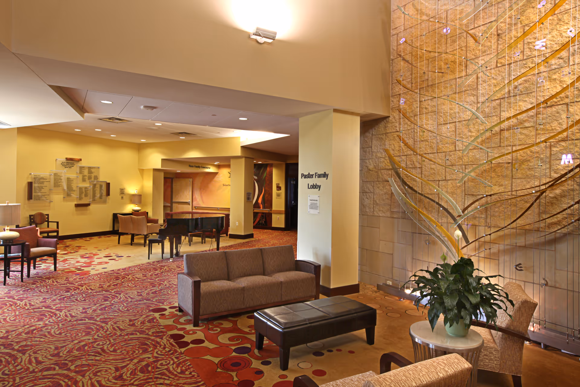 Spacious lobby with seating, a grand piano, patterned carpet, and a decorative glass wall sculpture.