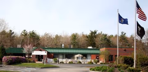 Exterior view of Maine Veterans' Home Bangor with flags and surrounding trees.