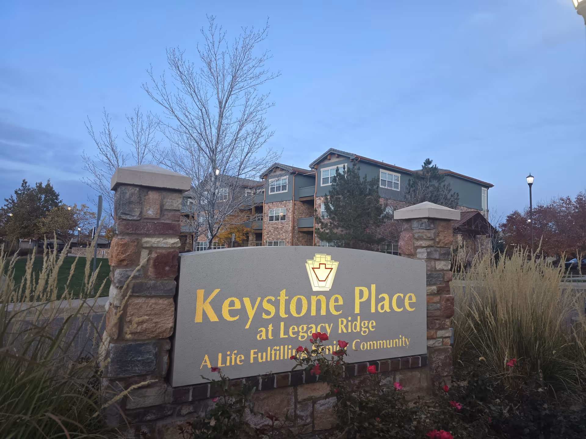 Entrance sign reading "Keystone Place at Legacy Ridge" in front of a multi-story assisted living building with landscaping.