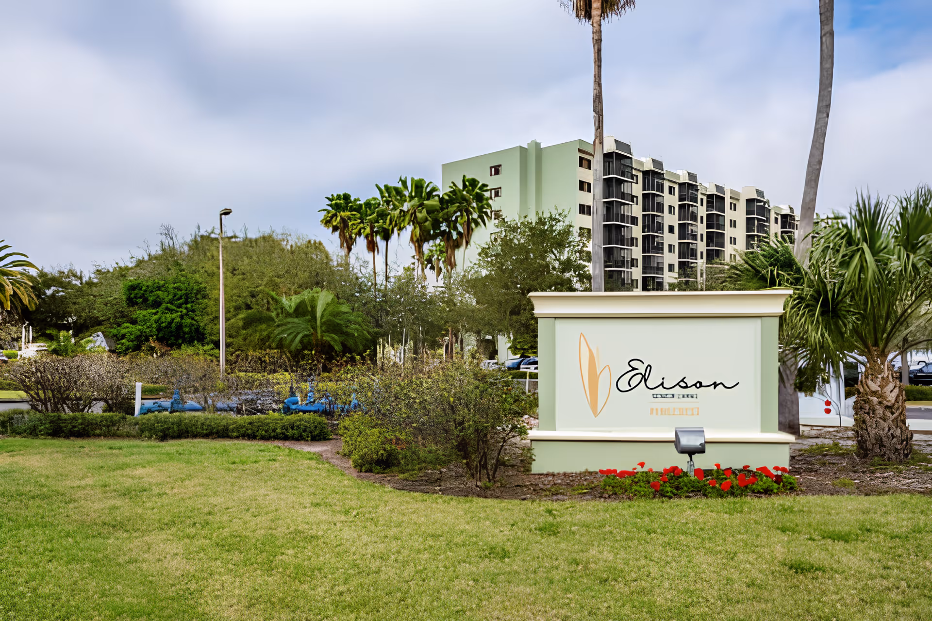 Entrance sign reading "Elison" on landscaped grounds with palm trees and a multi-story residential building in the background.