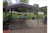 Outdoor patio area with a canopy tent, table, chairs, and railing overlooking a grassy field.