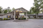 Exterior view of Perry County Nursing & Rehab Center showing the front entrance with a covered drop-off area, surrounded by trees and a paved driveway.
