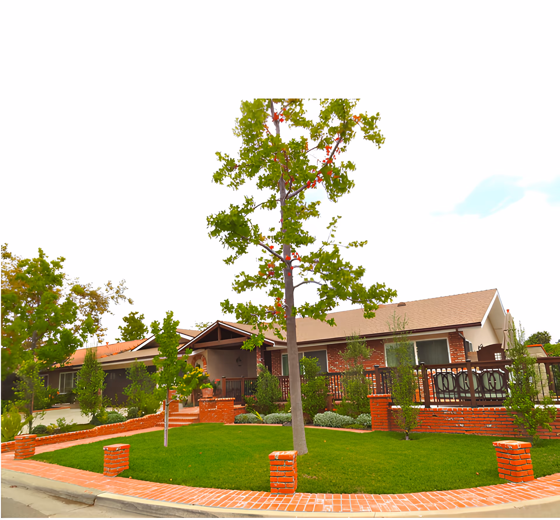 Exterior view of a single-story residential building with a brick facade and a beige roof. The front yard features a well-maintained green lawn, young trees, and brick landscaping elements including a low brick wall and brick pillars along the sidewalk. There is a covered porch area with steps leading up to the entrance.