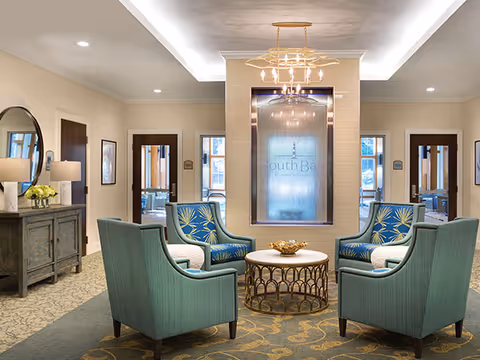 Elegant seating area with teal armchairs and a round coffee table in a senior living facility lobby.