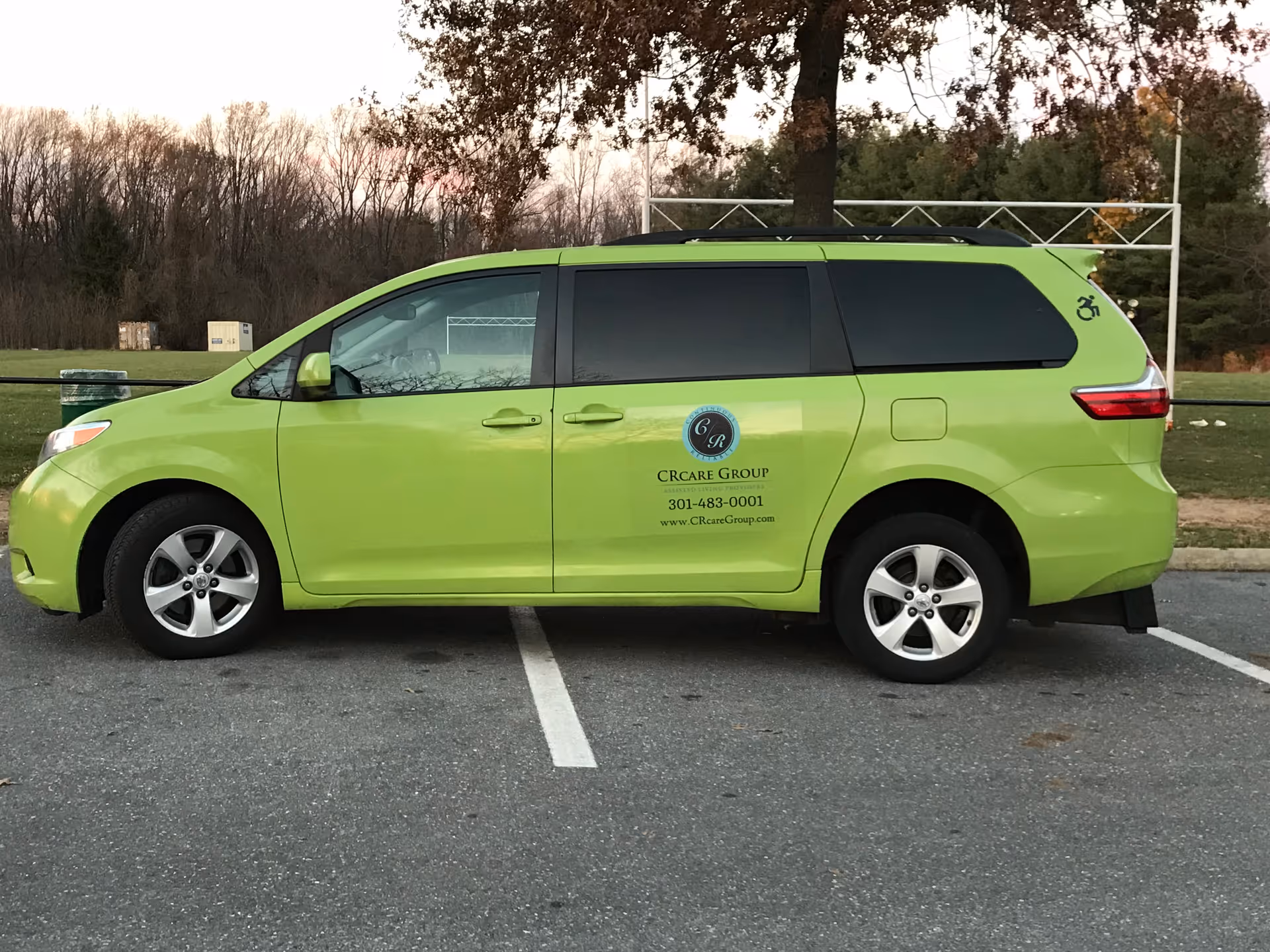 Chartreuse CR Care Group minivan with company logo parked in an outdoor lot in front of trees.
