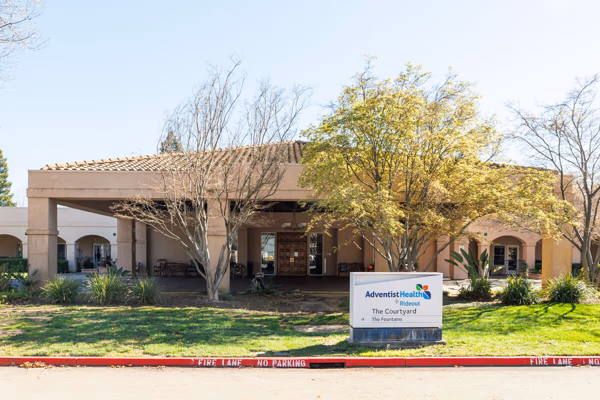 Front exterior view of The Courtyard Assisted Living building with a covered entry and a sign in the landscaped area.