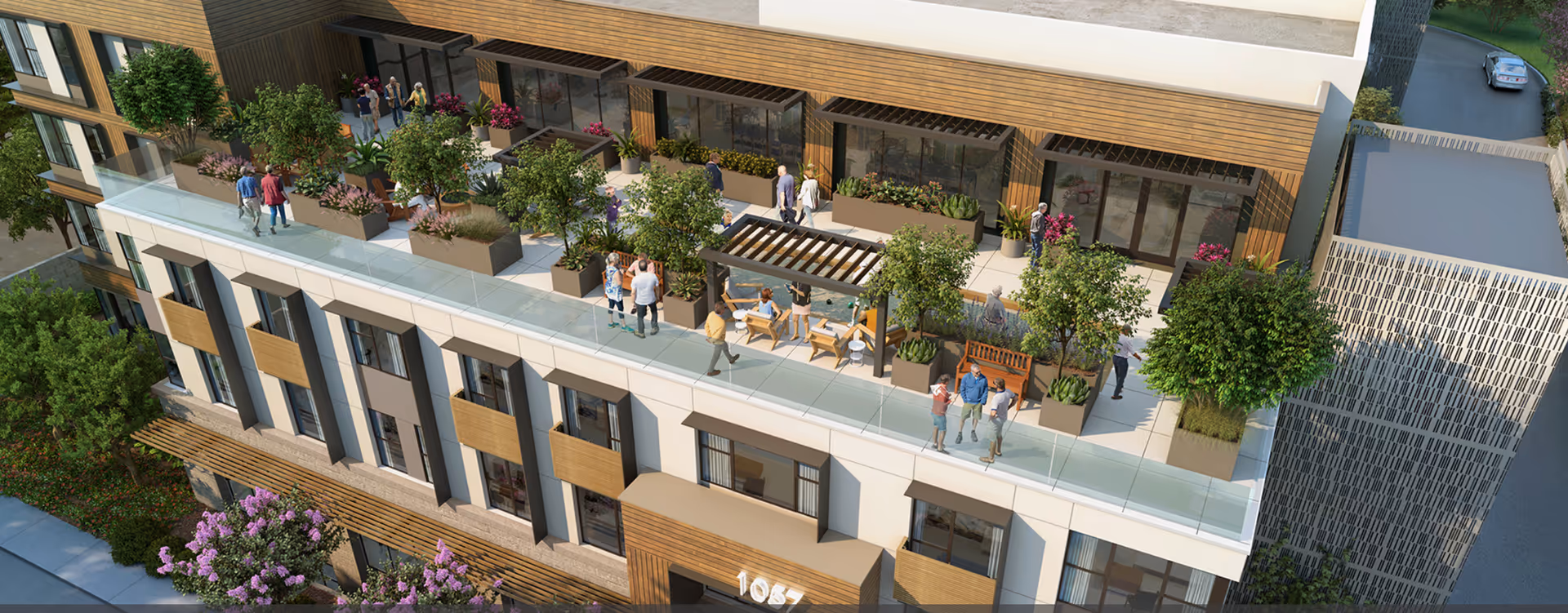Rooftop terrace on a modern multi-story building with planters, seating areas, and people gathered outdoors.