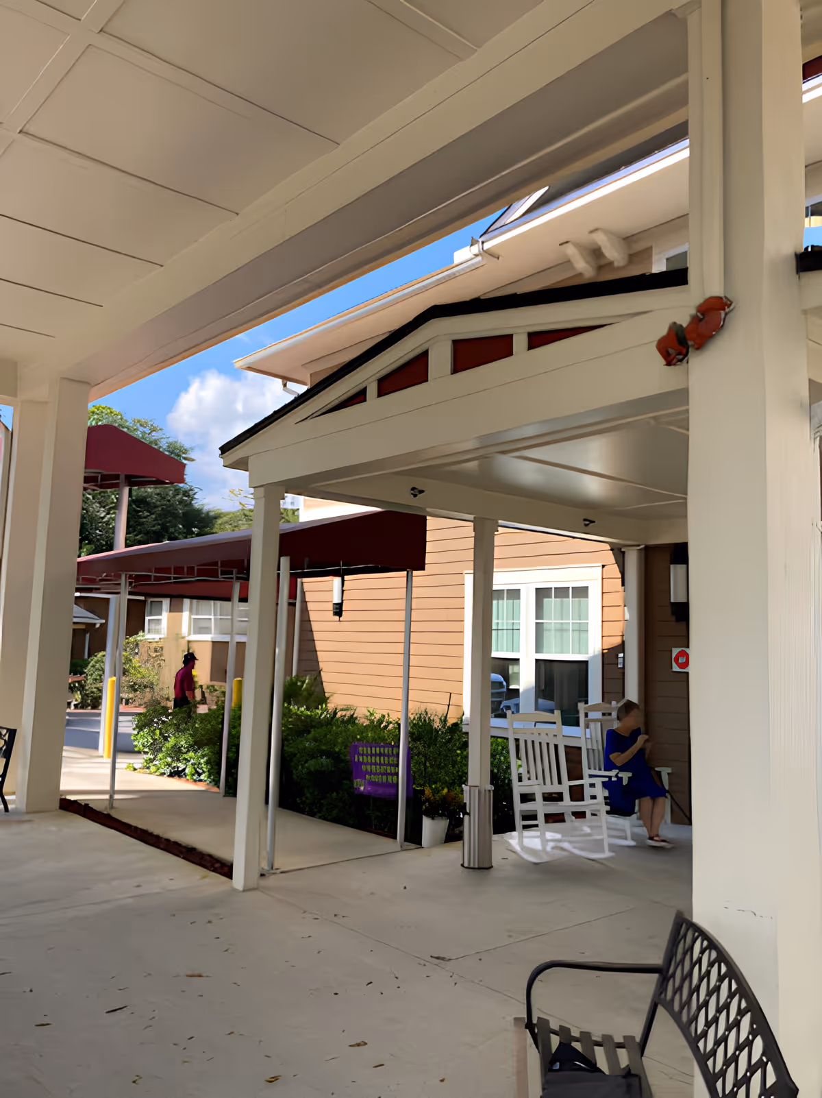 Covered entrance/porch area with white columns, awnings, rocking chairs, and a person seated near the building.