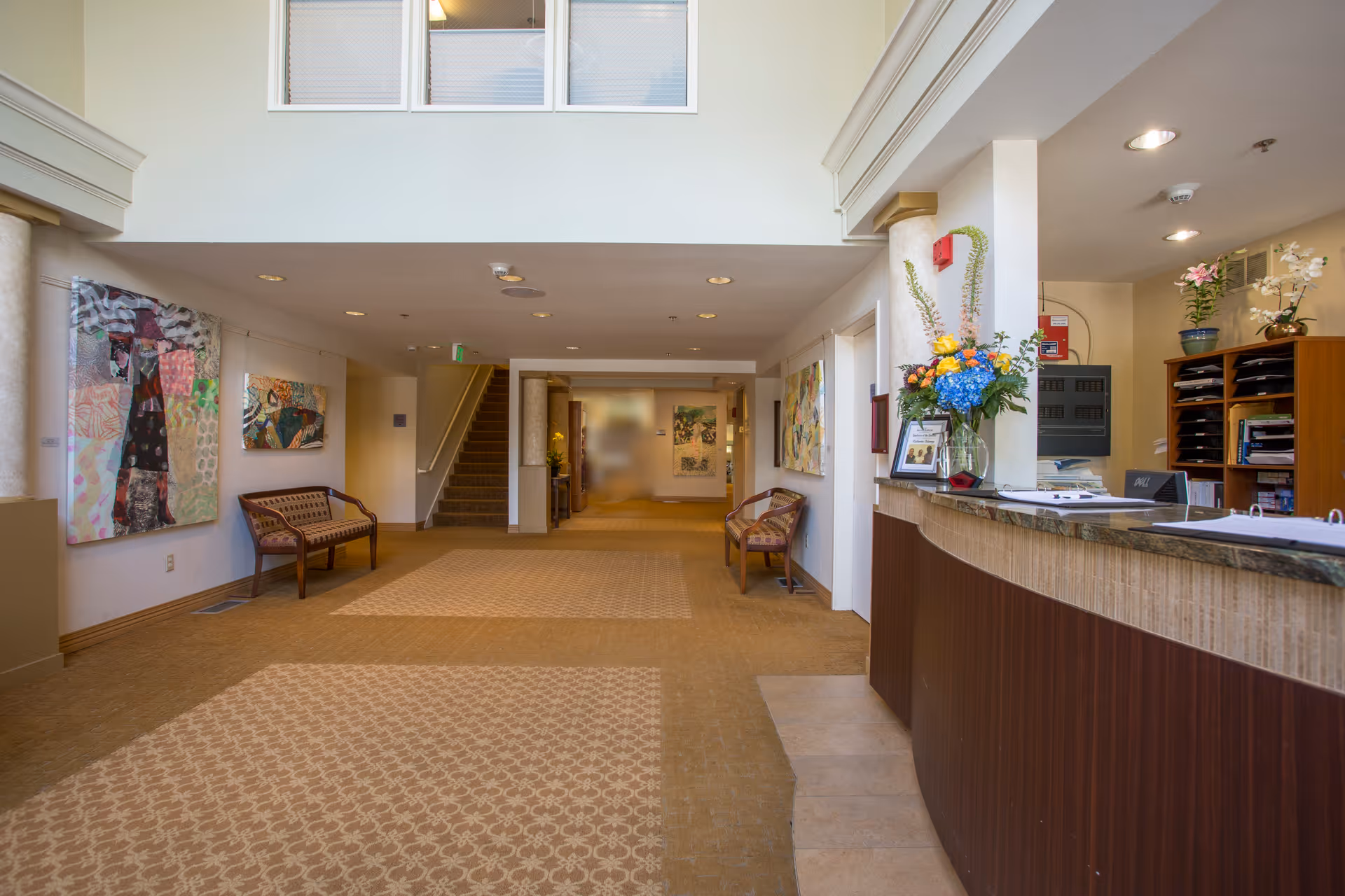 Bright reception lobby with a curved front desk, seating benches, artwork on the walls, and a central hallway.