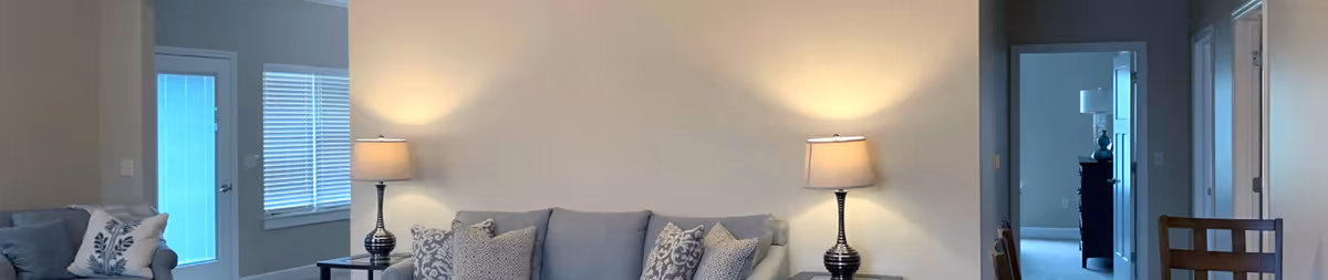 Neutral living room with a gray sofa flanked by two table lamps, decorative pillows, and doorways leading to adjacent rooms.