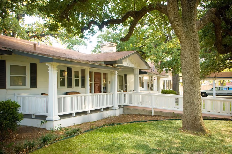 Exterior view of Romberg House Assisted Living: white, single-story building with a wraparound porch.