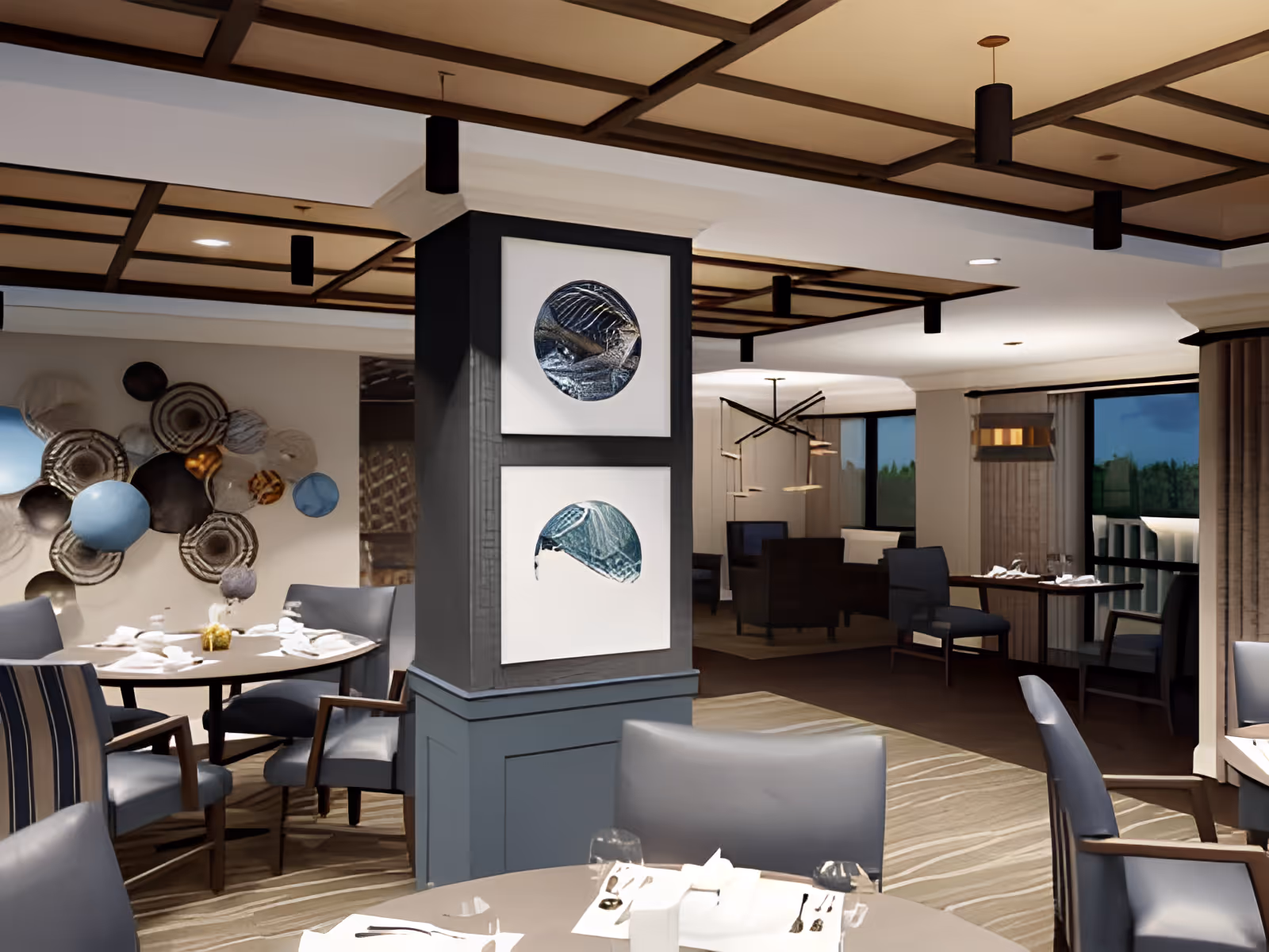 Contemporary dining room with round set tables and upholstered chairs, decorative wall art, and a central column displaying framed artwork.