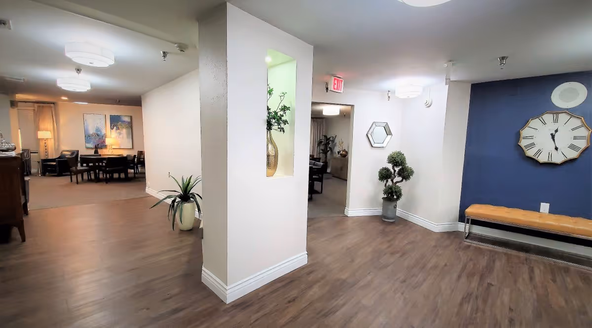 Lobby-style interior with wood floors, seating areas, decorative plants, wall clock and bench.