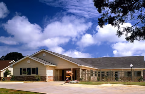 Single-story retirement community building with beige siding under a blue sky.
