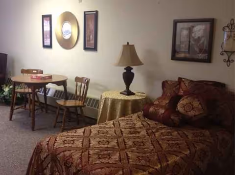 A cozy senior living suite with a bed, table, chairs, and decorative wall art.