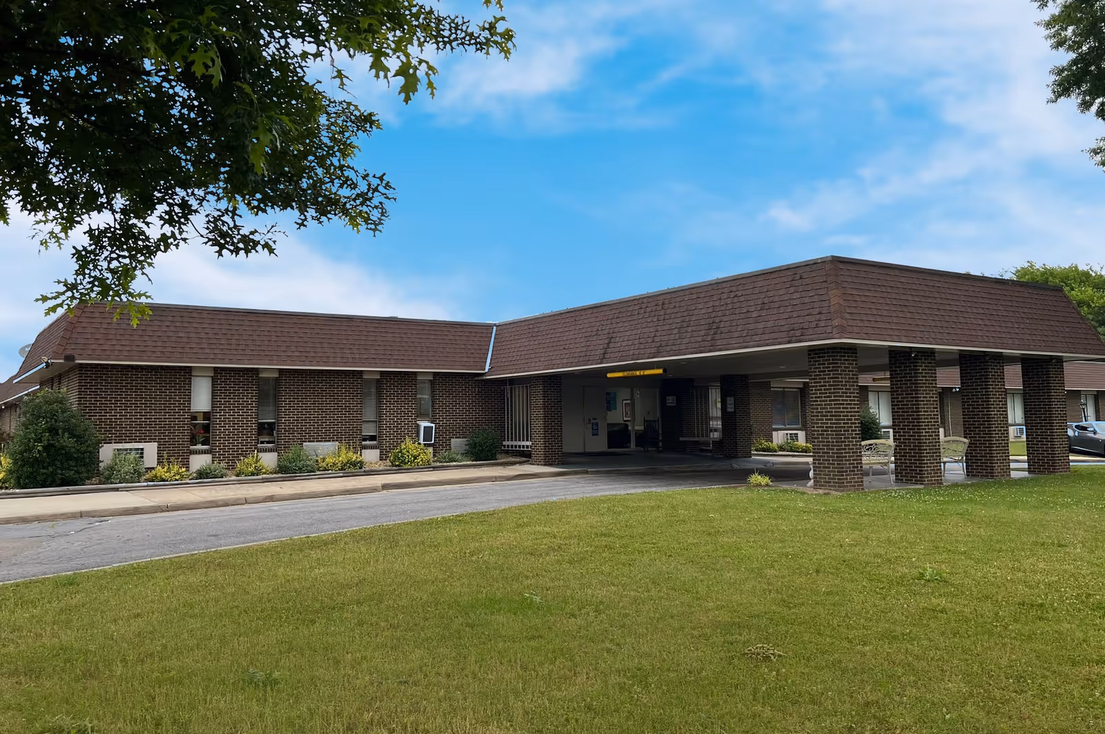 Exterior view of a brick senior care facility with a covered entrance and green lawn.