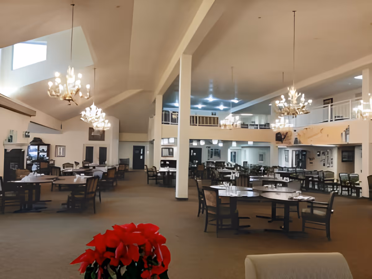 Large dining room with multiple round tables and chandeliers and a red poinsettia in the foreground.