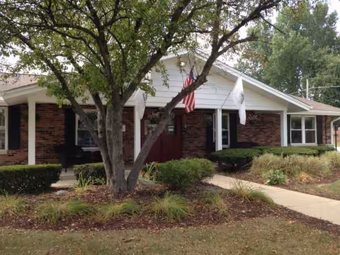 Front exterior of a brick senior living center with flags and landscaping.