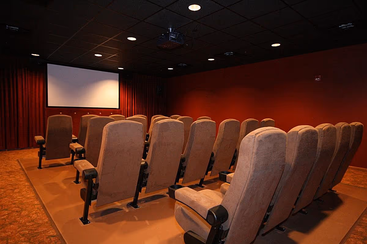 Small screening room with rows of upholstered theater seats facing a projection screen.
