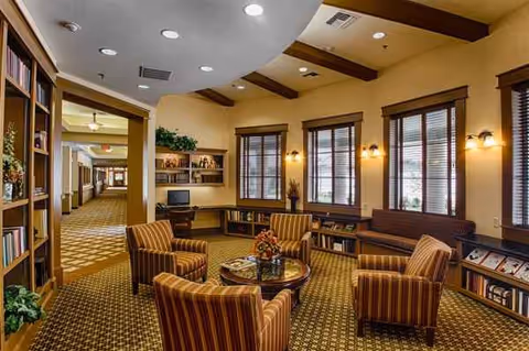 Warmly lit senior living lounge with striped chairs, tables, and bookshelves.