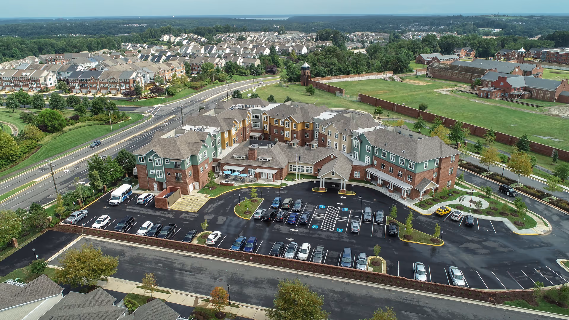 Aerial view of a multi-story senior living building with a curved driveway, parking lot and surrounding residential neighborhood.