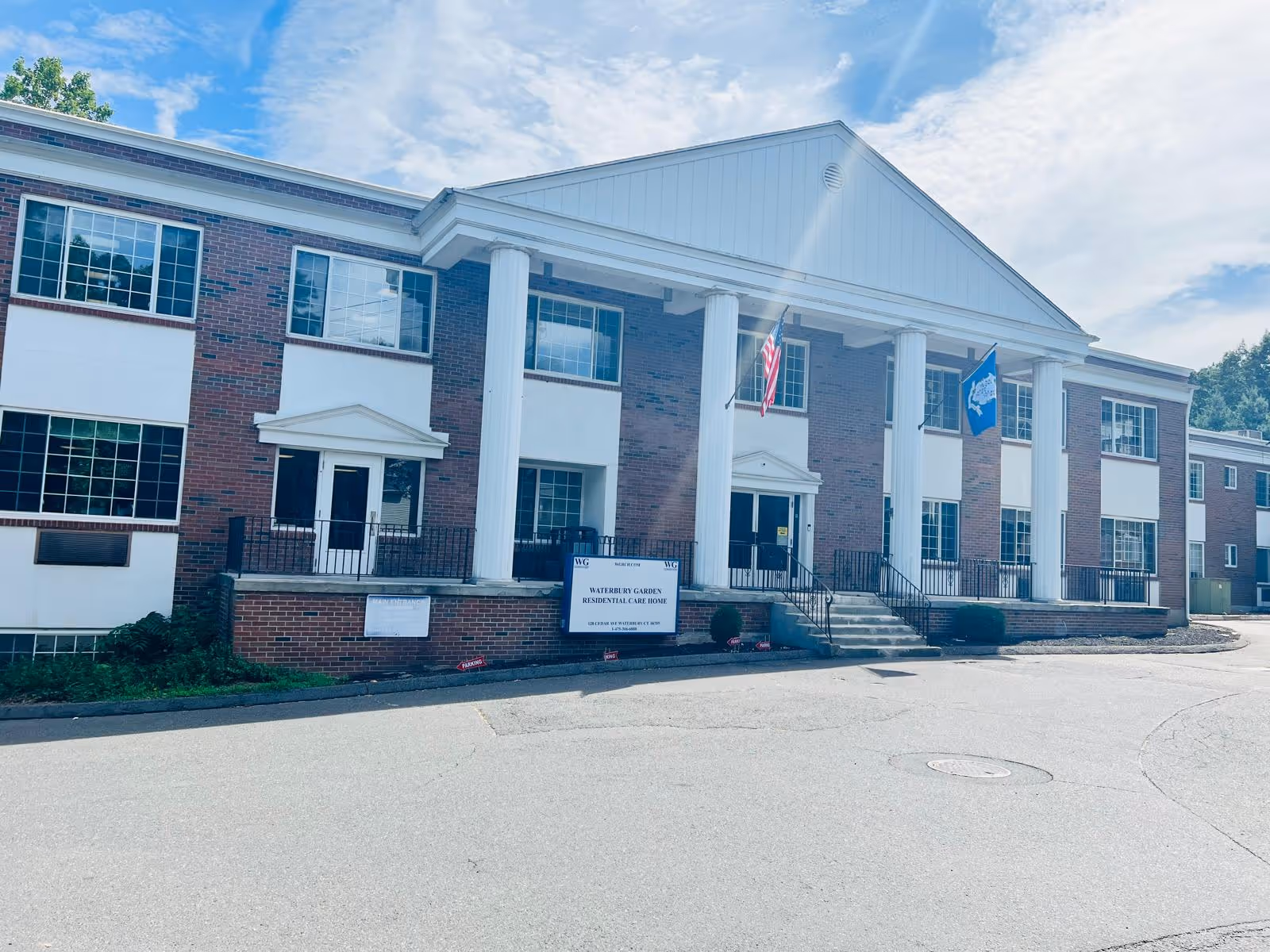 Exterior view of Waterbury Gardens senior living facility with a brick facade and flags.