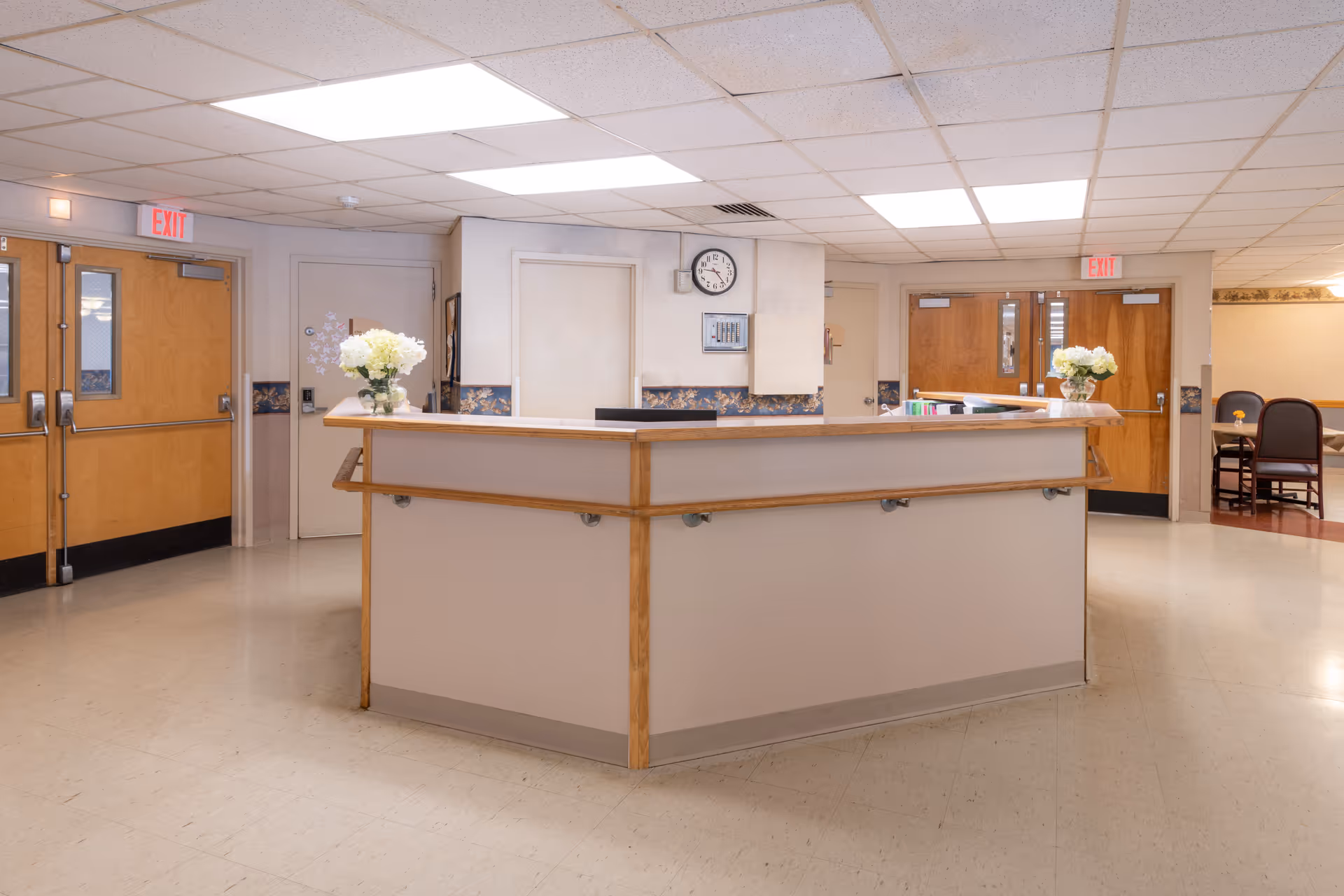 Reception desk and nursing station in a senior living facility lobby with flowers and double exit doors.
