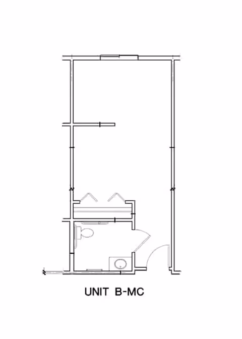 Architectural floor plan labeled UNIT B-MC showing a layout with a bathroom area including a toilet and sink, and an adjoining larger room.
