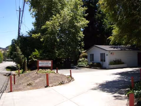 Small, single-story facility entrance with trees and a paved driveway.