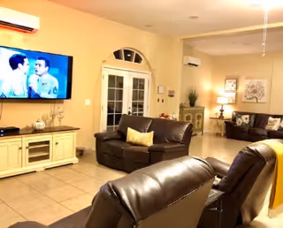 Open living room with brown leather seating, a wall-mounted TV, tiled floor, and French doors.